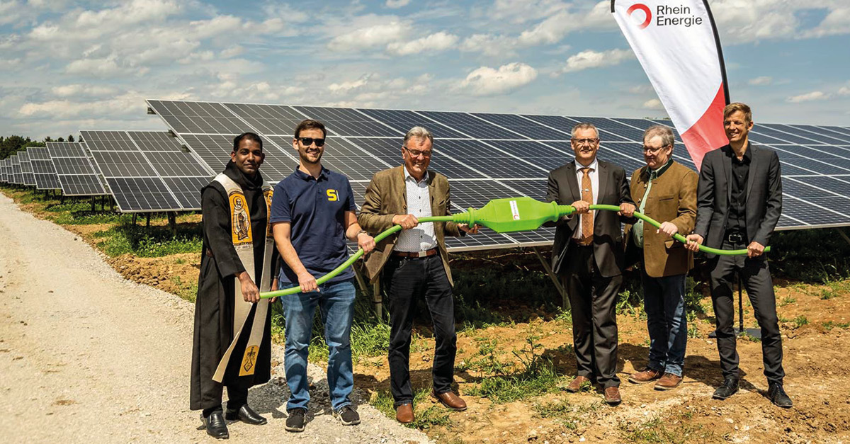 Im Bild zu sehen sind fünf Männer mit einem großen Stromkabel: Pfarrvikar Santosh Thomas, Sebastian Kögel von GOLDBECK SOLAR, Hans Pollinger (Erster Bürgermeister Hemau a.D.), Herbert Tischhöfer (Erster Bürgermeister Hemau), Johann Kaffler (Landwirt), Ulrich Bemmann (RheinEnergie)